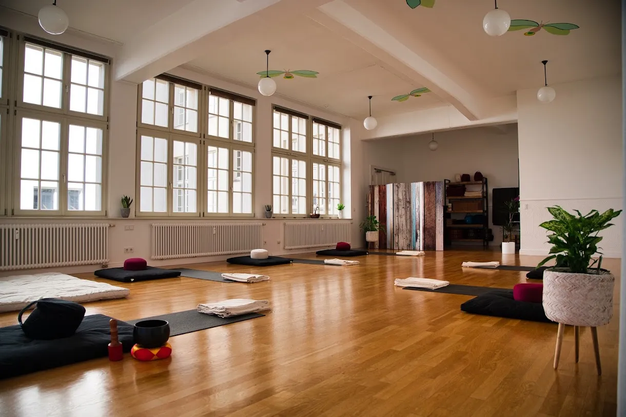 Kursraum in Leipzig vor Kursbeginn: vorbereitete Plätze mit Matte, Meditationskissen und gefalteter Decke, hohe Fenster mit Tageslicht
