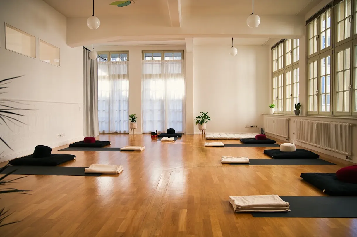 Heller Kursraum in Leipzig, für einen MBSR-Kurs vorbereitet: Matten mit Meditationskissen und gefalteten Decken, hohe Fenster mit Tageslicht